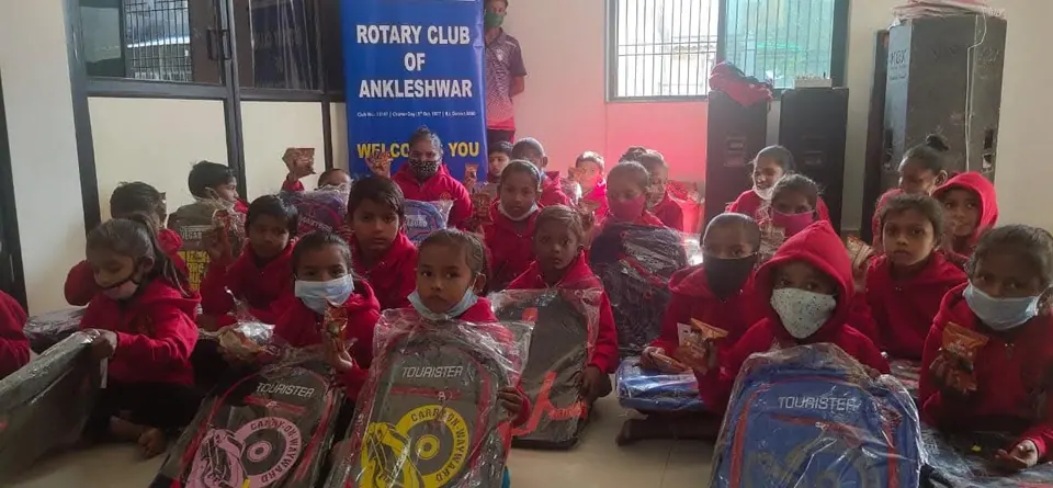 Children in red jackets with gift bags, Rotary Club of Ankleshwar banner